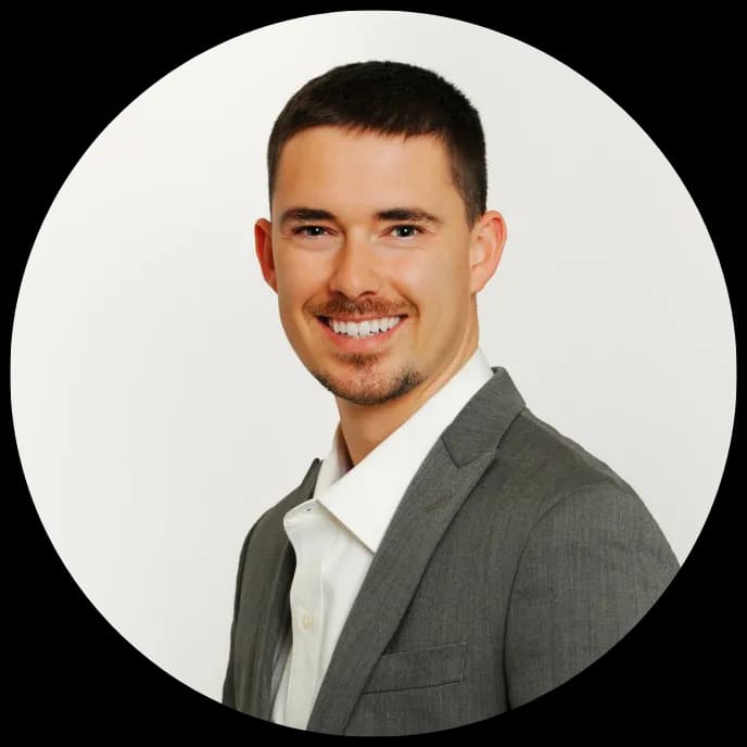 Smiling man with short brown hair and goatee wearing a grey suit and white shirt.