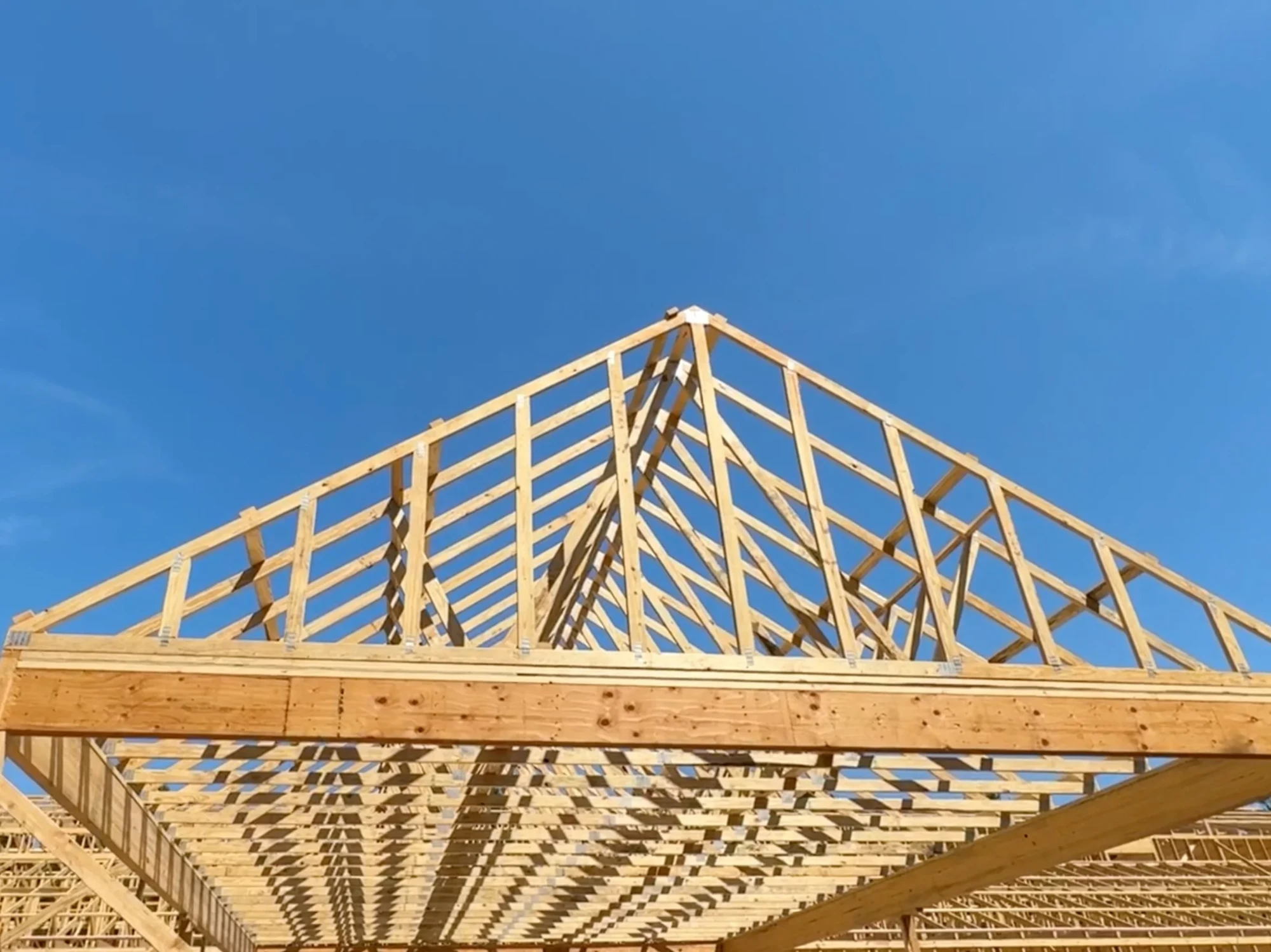 Wooden roof trusses framing the roof of a building under construction against a clear blue sky